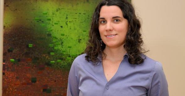 A woman poses for a photo in front of a piece of art. 